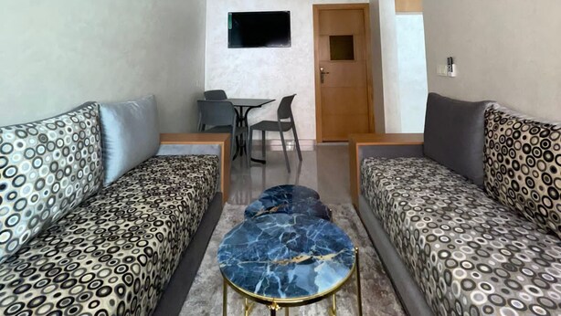 Ein gemütlicher Wohnraum mit zwei gemusterten Sofas, einem kleinen runden Tisch, einem an der Wand befestigten Fernseher und einer Tür zu einem weiteren Zimmer.