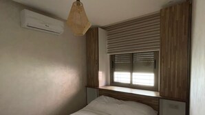 Ein Schlafzimmer mit einem Bett, einer Klimaanlage, einem Fenster mit Jalousien und einer Pendelleuchte.