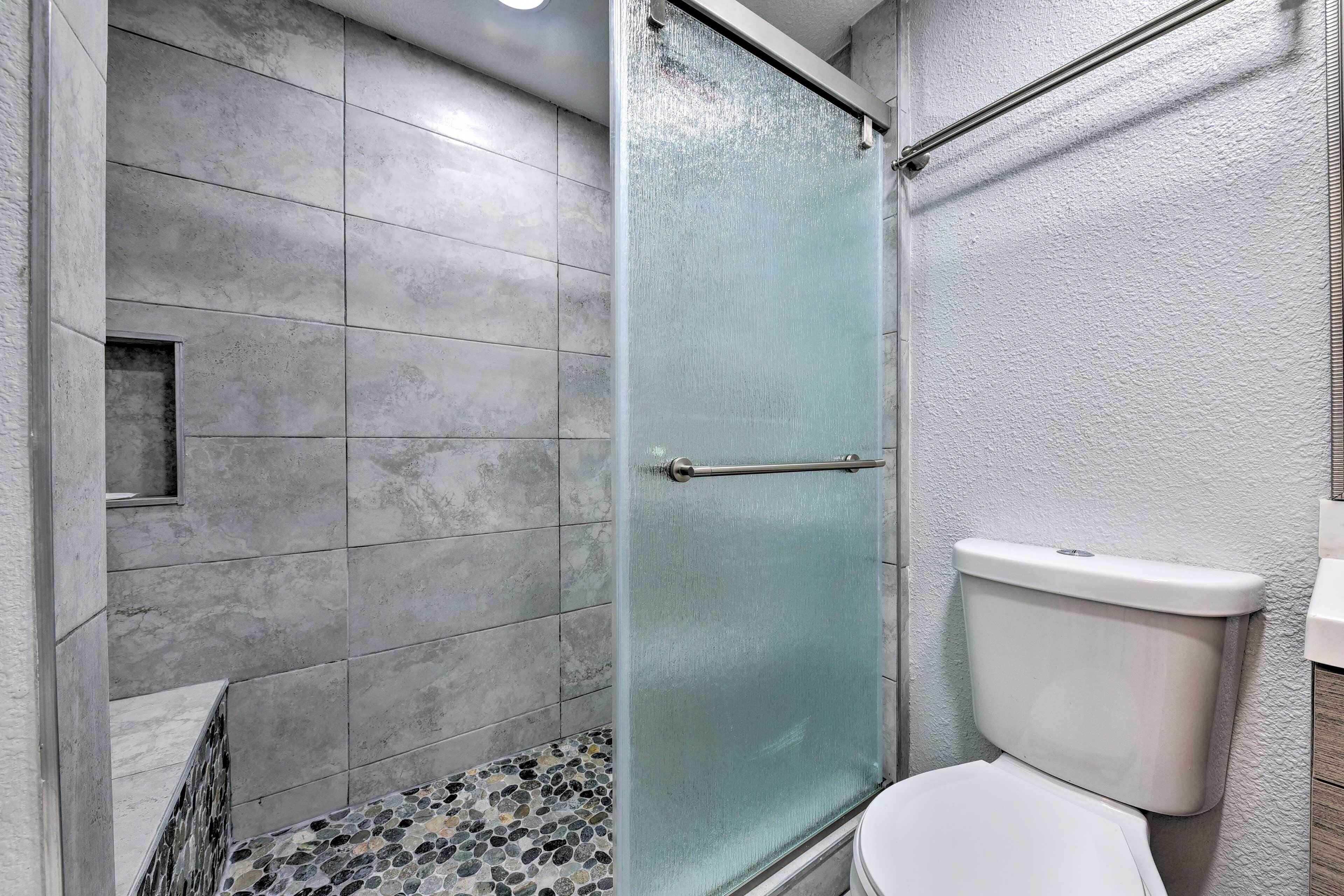 A bathroom with a glass shower enclosure, a toilet, and tiled flooring.