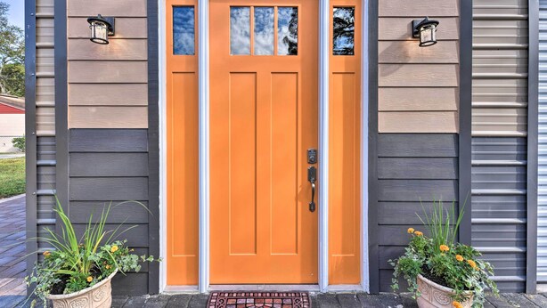 A house with a bright orange front door, two wall-mounted lights, and two potted plants on either side. - Cozy Jacksonville Studio - 10 Miles to Downtown! (Jacksonville)