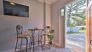 A room with a TV mounted on the wall, two metal chairs with cushioned seats, a small table, and a door leading to an outdoor area with a brick pathway and greenery. - Cozy Jacksonville Studio - 10 Miles to Downtown! (Jacksonville)