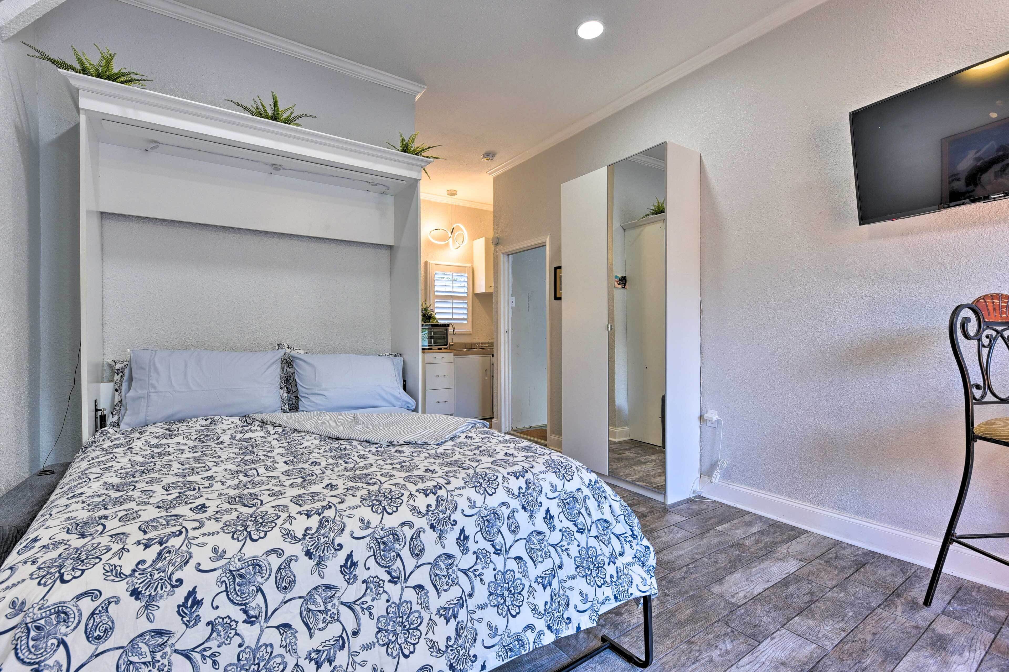 Un dormitorio con una cama grande, un televisor montado en la pared y un pasillo que conduce a otras habitaciones.