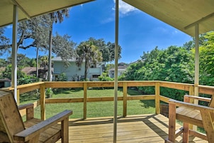 A wooden deck with a railing, overlooking a grassy yard with trees and a house in the background.