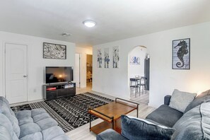 Een moderne woonkamer met een flatscreen televisie, een grijze bank, een kamerkleed met dessin en kunstwerken aan de wanden.