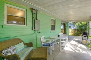 Een overdekt terras met een groene wand, rieten meubels, een tafel en een barbecue.