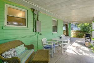 Un patio techado con pared verde, muebles de mimbre, una mesa y una parrilla.