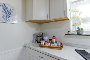 Een keuken met witte kasten, een koffiezetapparaat, een schaal met snacks en een raam met een orchidee.