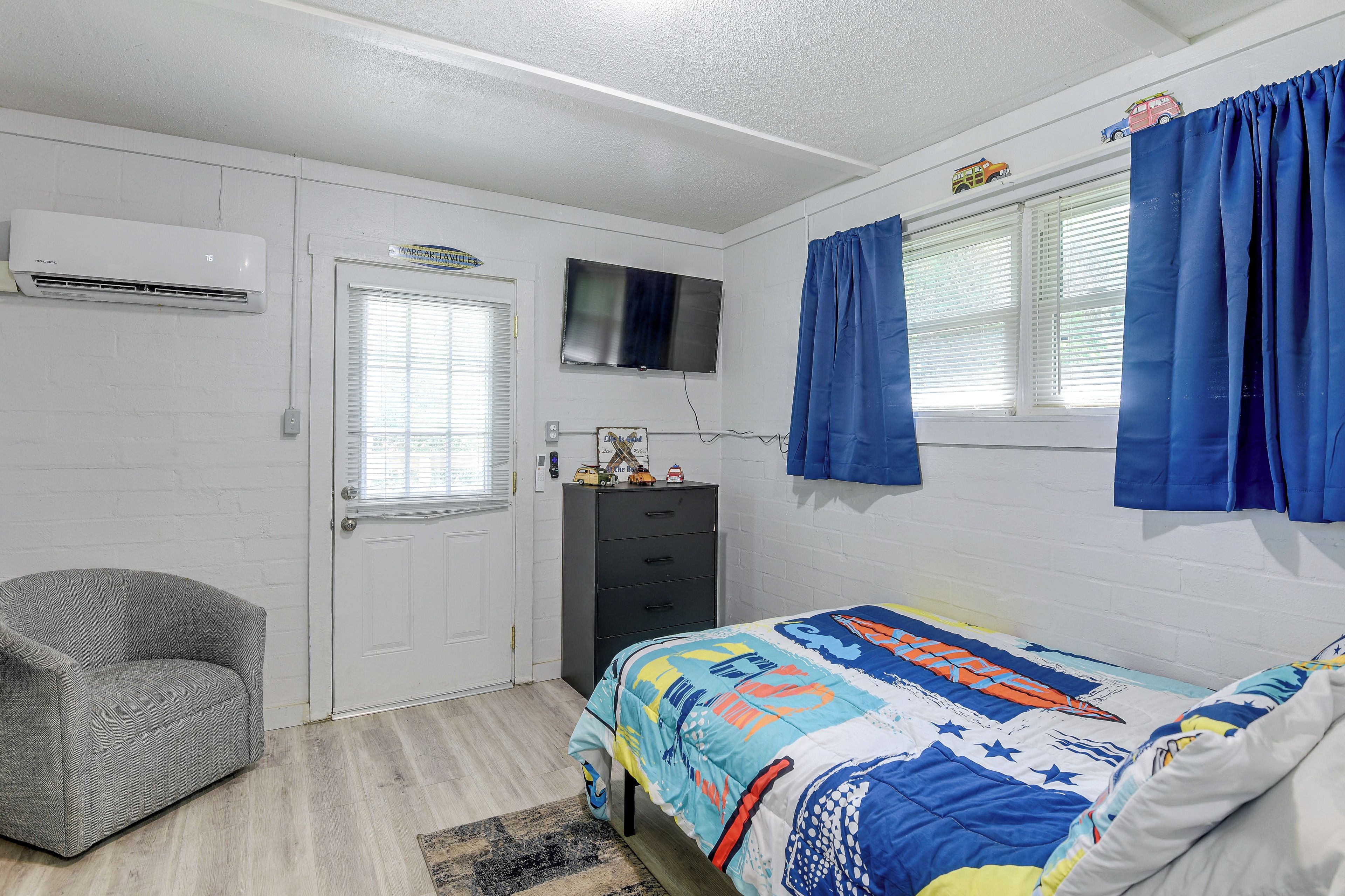 A bedroom with a bed, a chair, a dresser, a TV, and a window with curtains.