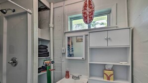 Ein Badezimmer mit Dusche, Waschbecken und Spiegel. Ein Handtuchhalter mit Handtüchern und eine Taschentuchbox befinden sich auf den Regalen.