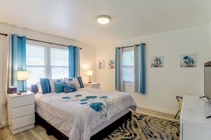 Un dormitorio con cama, mesitas de noche, lámpara y ventana con cortinas.