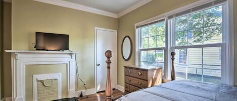 A bedroom with a fireplace, a bed, a dresser, and a television.