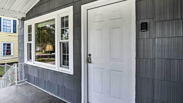 A house with a grey siding exterior, a white front door, and a window with a white frame.