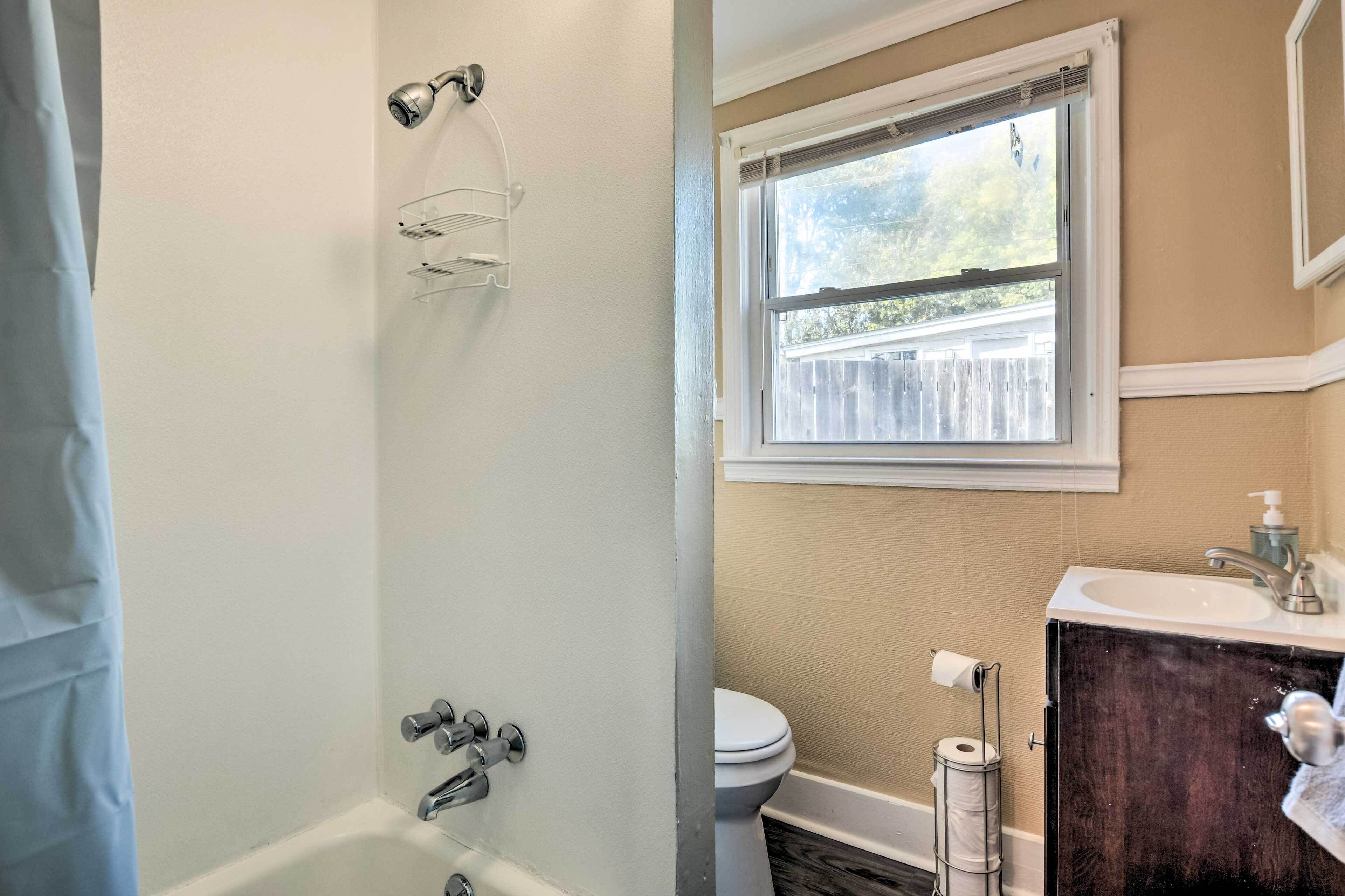 A bathroom with a bathtub, a toilet, a window, and a sink with a mirror.