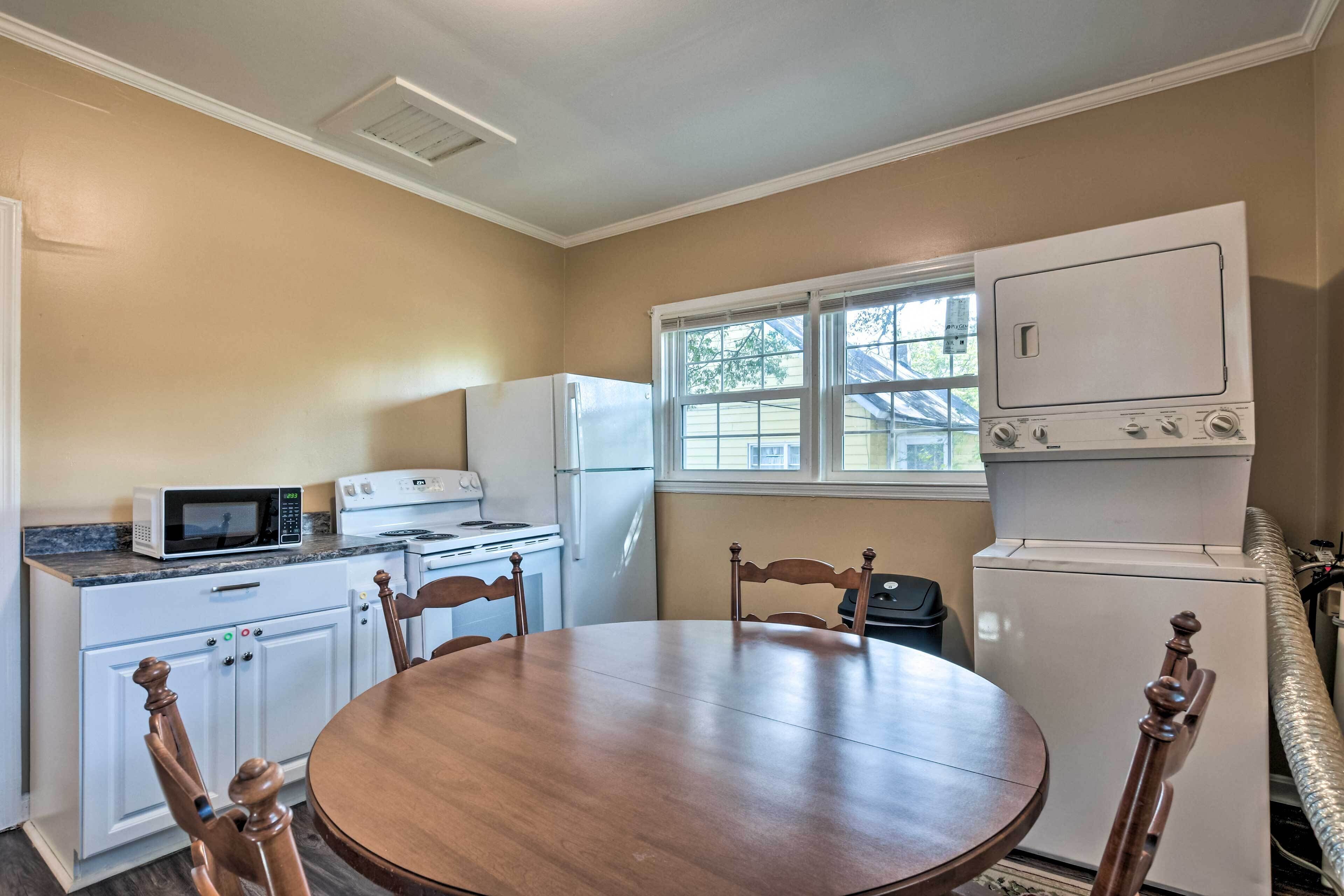 A compact kitchen with white appliances, a dining table, and wooden chairs.