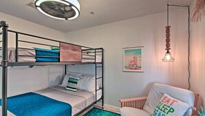 En køjeseng med et blåt lagen, en træstol med en pude, og en hængende lampe.