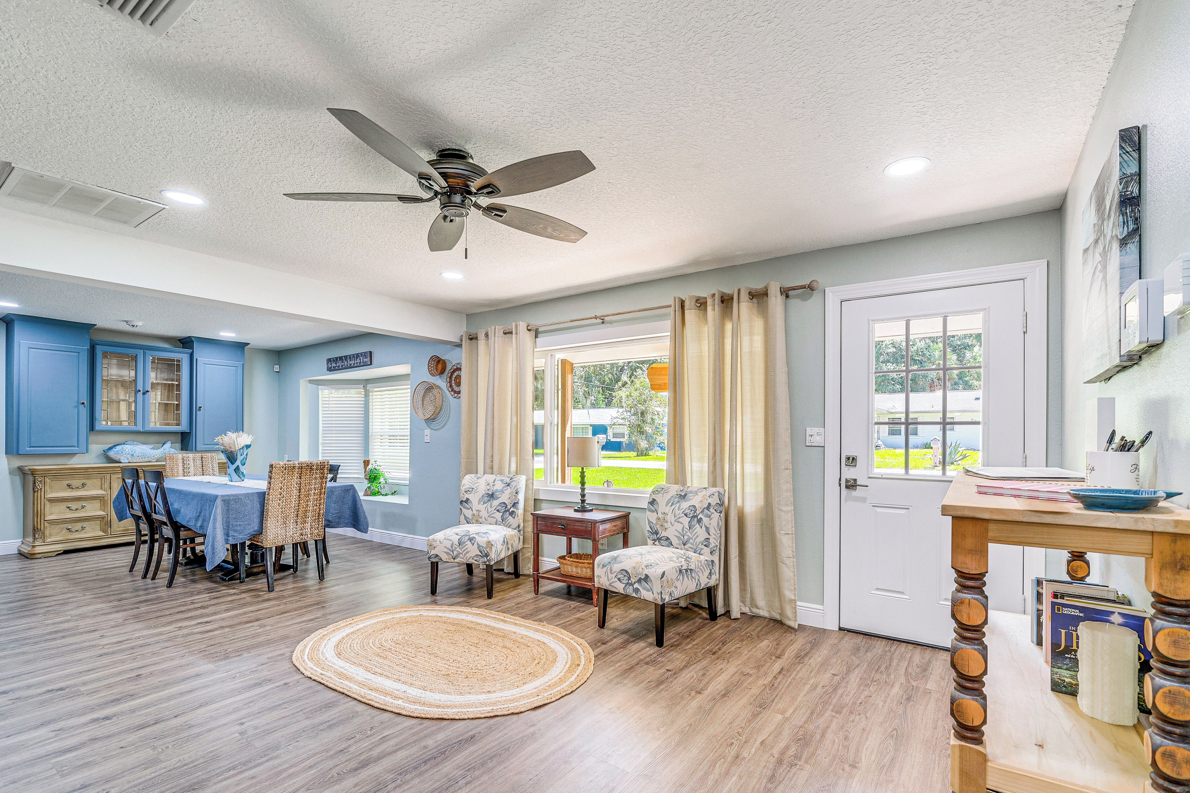 A spacious living room with a dining area, a ceiling fan, and a view through a door to the outdoors.