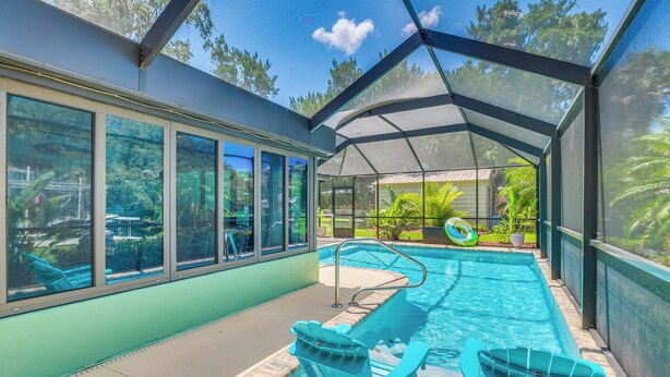 A covered outdoor swimming pool with lounge chairs and a view of the surrounding greenery. - Canal-front Outdoor Oasis: Home in Crystal Water (Crystal River)