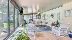 A sunlit living room with wicker furniture, a glass door leading outside, and a television mounted on the wall. - Canal-front Outdoor Oasis: Home in Crystal Water (Crystal River)