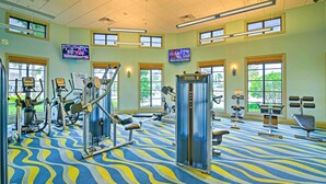 Ein Fitnessstudio mit verschiedenen Trainingsgeräten, großen Fenstern und einem gemusterten Teppich.