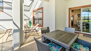 Eine Terrassenfläche mit Tisch und Stühlen, eine Schiebetür und Blick ins Grüne.