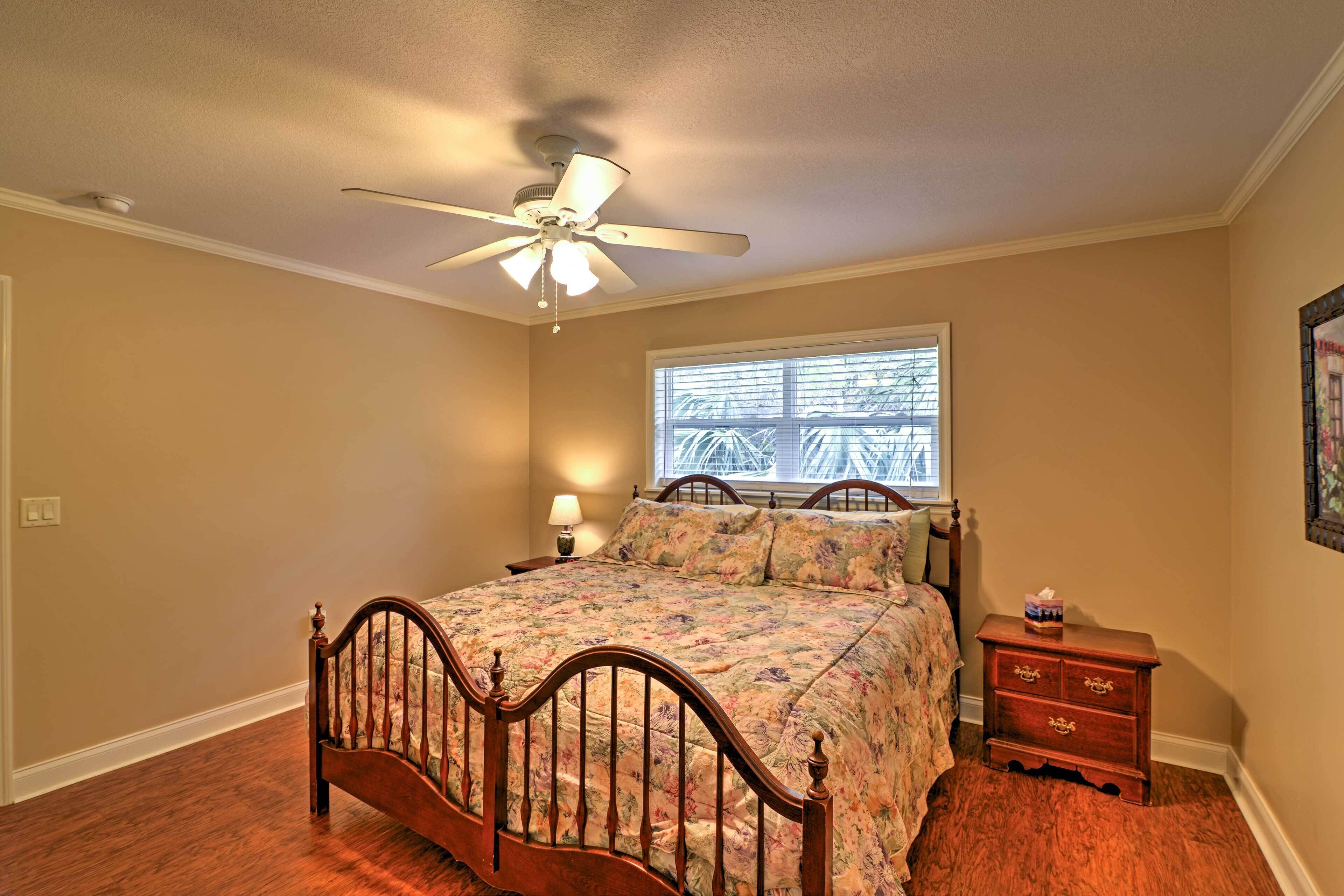 A bedroom with a wooden bed, a ceiling fan, a window with blinds, and a nightstand.