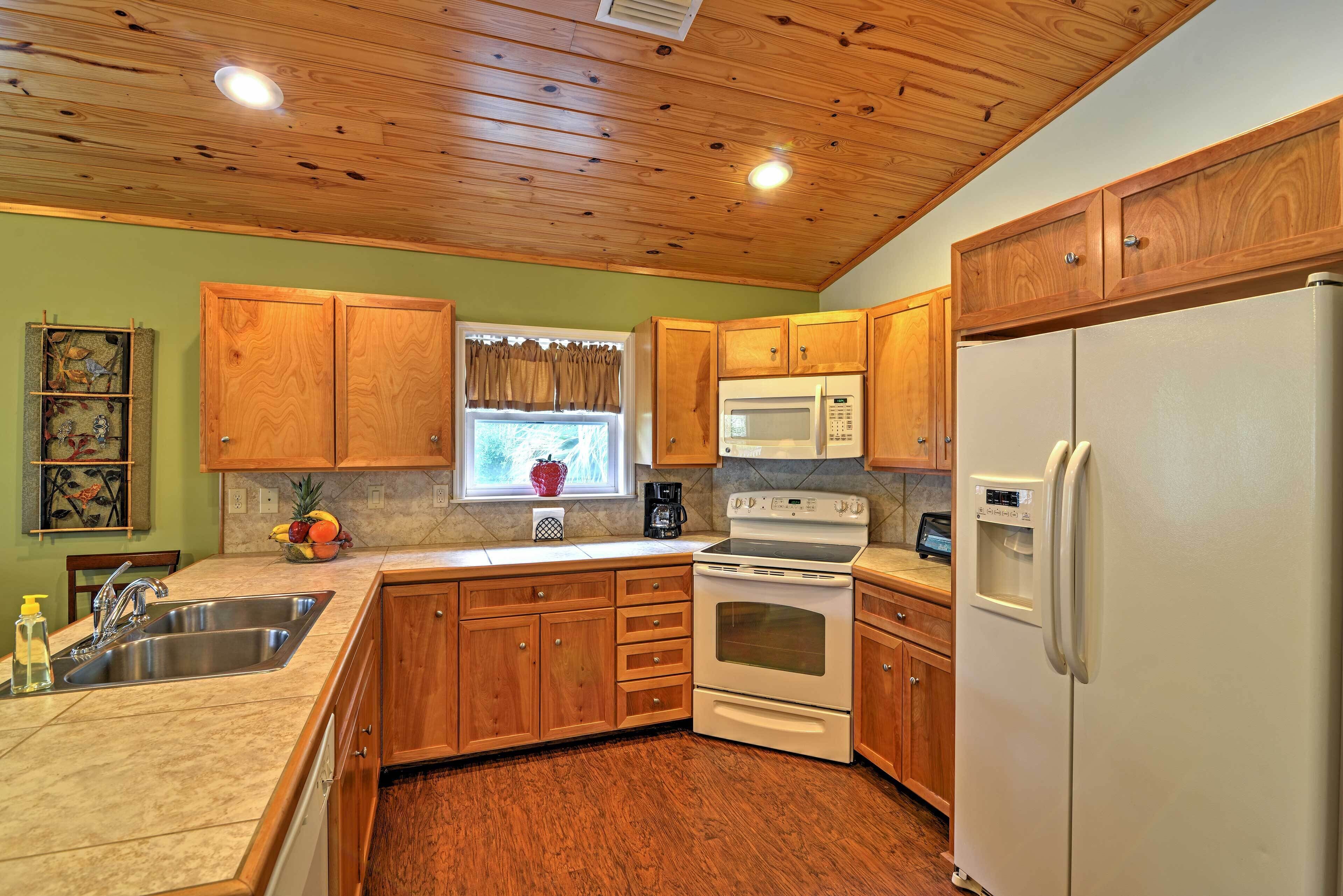 A kitchen with wooden cabinets, a stainless steel sink, a microwave, an oven, and a refrigerator.