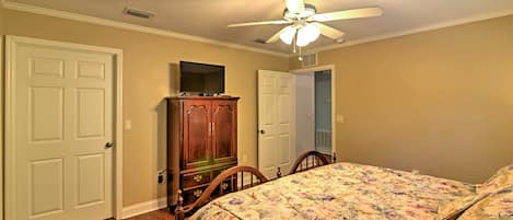 A bedroom with a bed, a wooden dresser, a ceiling fan, and two doors.
