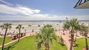 A beach view from a hotel balcony with palm trees, lounge chairs, and a flag. - Daytona Beach Studio w/ Oceanfront Balcony & Pool! (Daytona Beach)