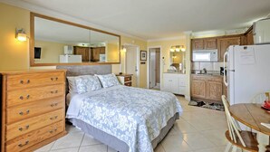 A bedroom with a large bed, a dresser, and a mirror. There is a kitchenette with a microwave, refrigerator, and sink. - Daytona Beach Studio w/ Oceanfront Balcony & Pool! (Daytona Beach)