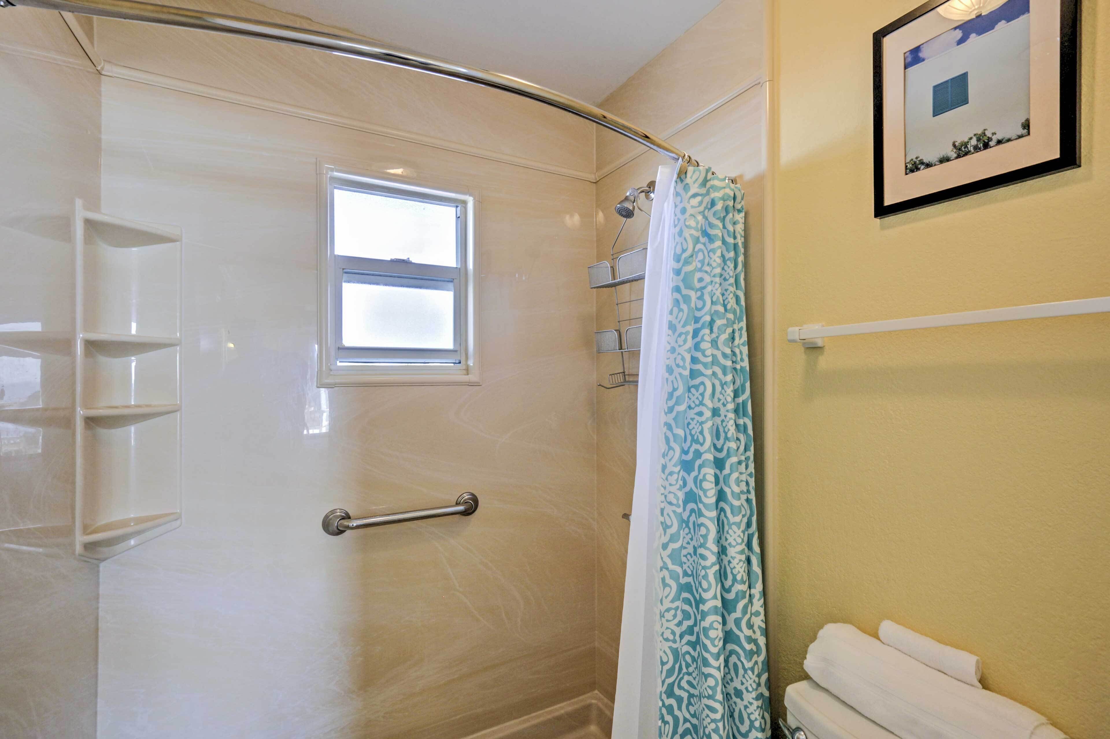 A shower with a glass door, a window, a towel rack, and a framed picture on the wall.
