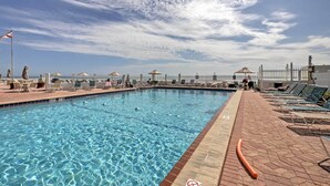 A swimming pool with clear water, surrounded by lounge chairs and umbrellas, and a fenced area with a gazebo. - Daytona Beach Studio w/ Oceanfront Balcony & Pool! (Daytona Beach)