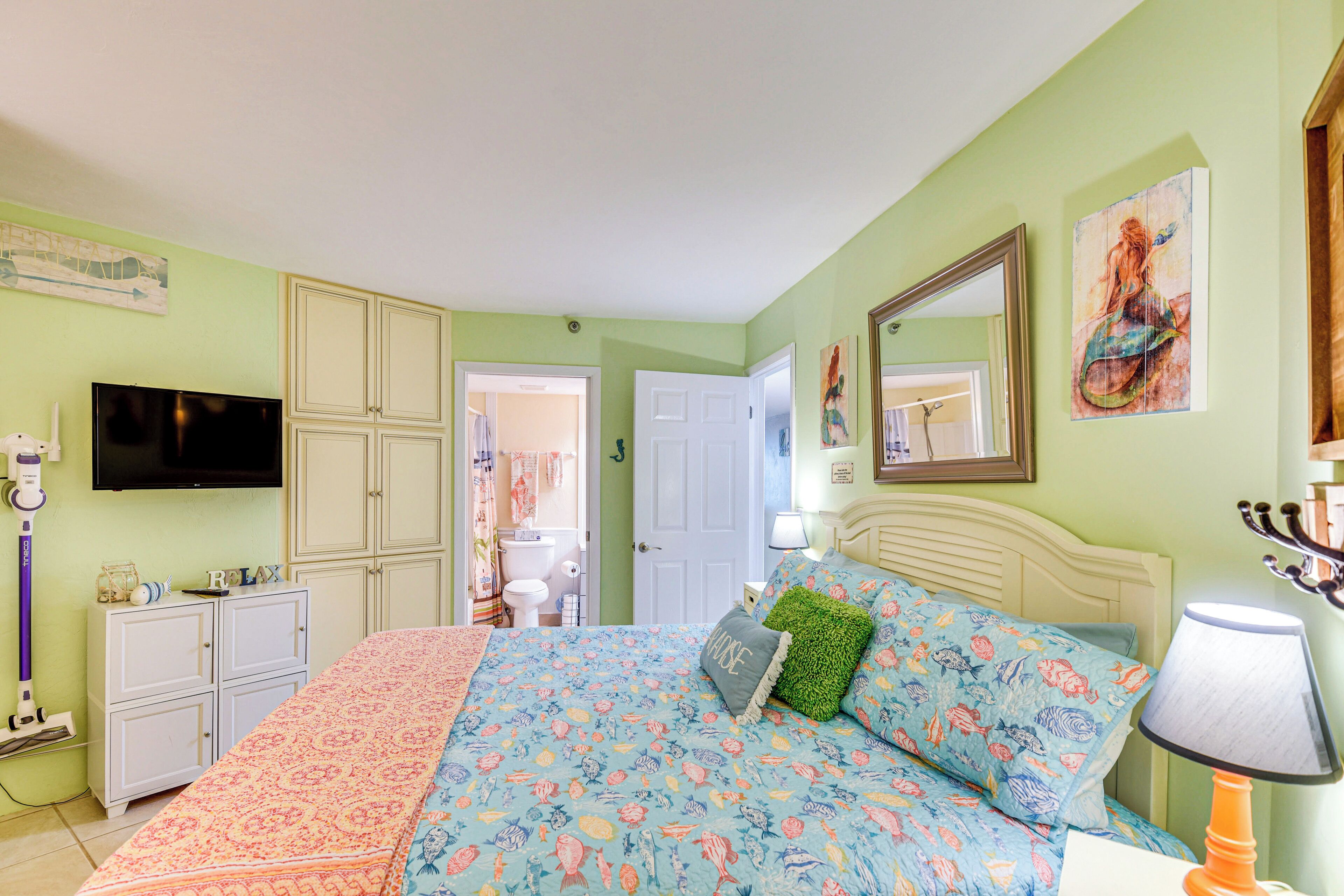 A bedroom with a bed, a TV, a cabinet, and a bathroom door.
