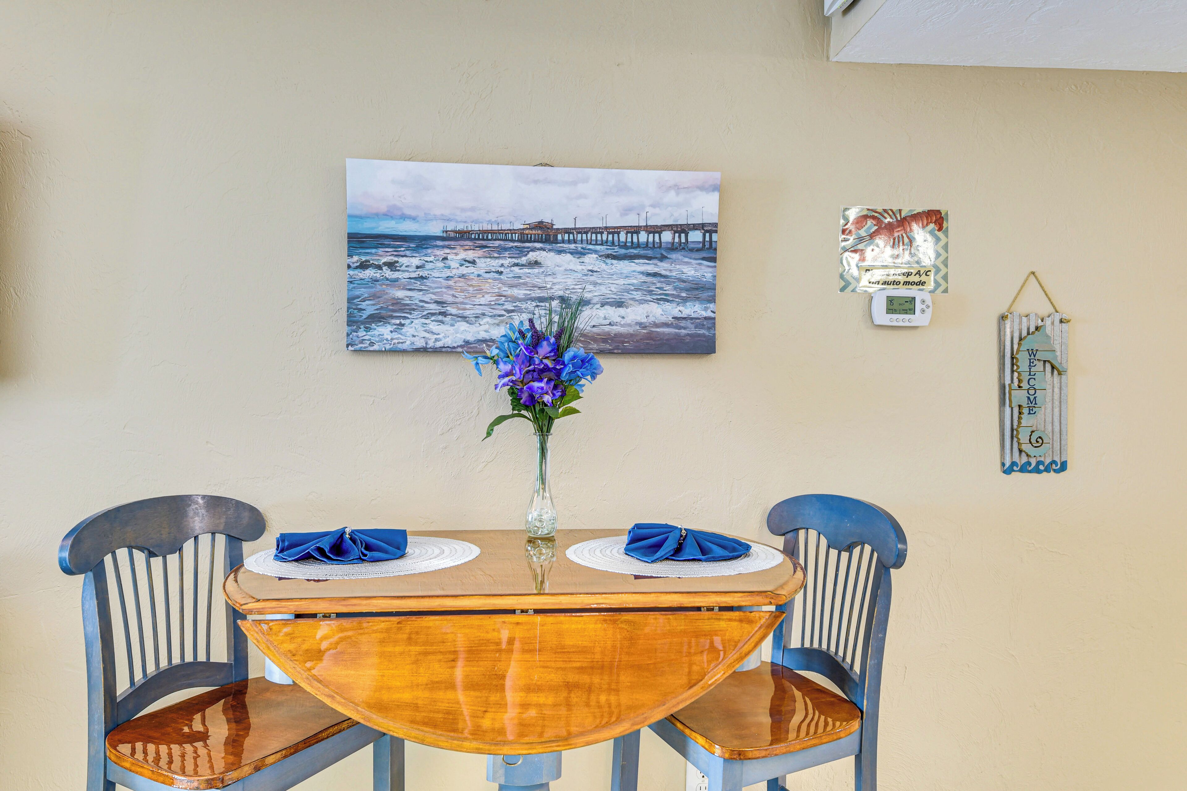Una mesa de comedor con dos sillas, un florero con flores y un cuadro de un muelle en la pared.