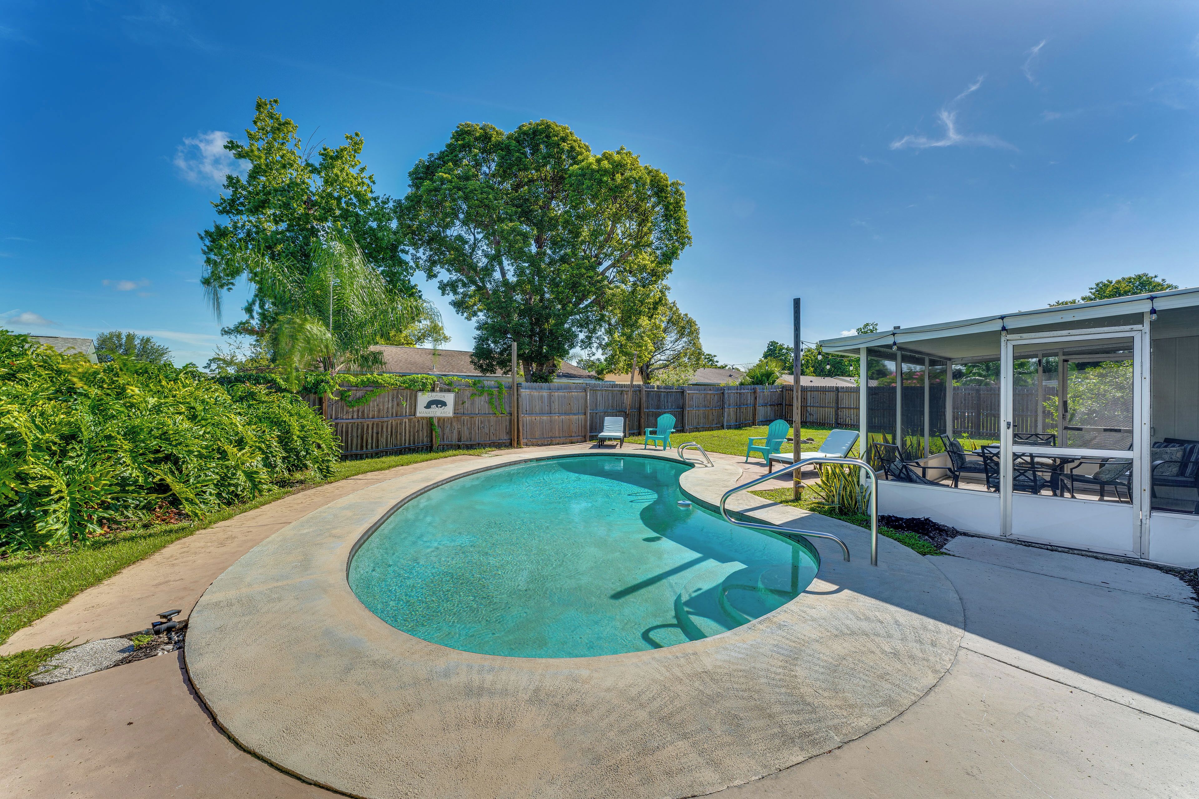 A backyard with a swimming pool, a covered patio area, and a wooden fence.