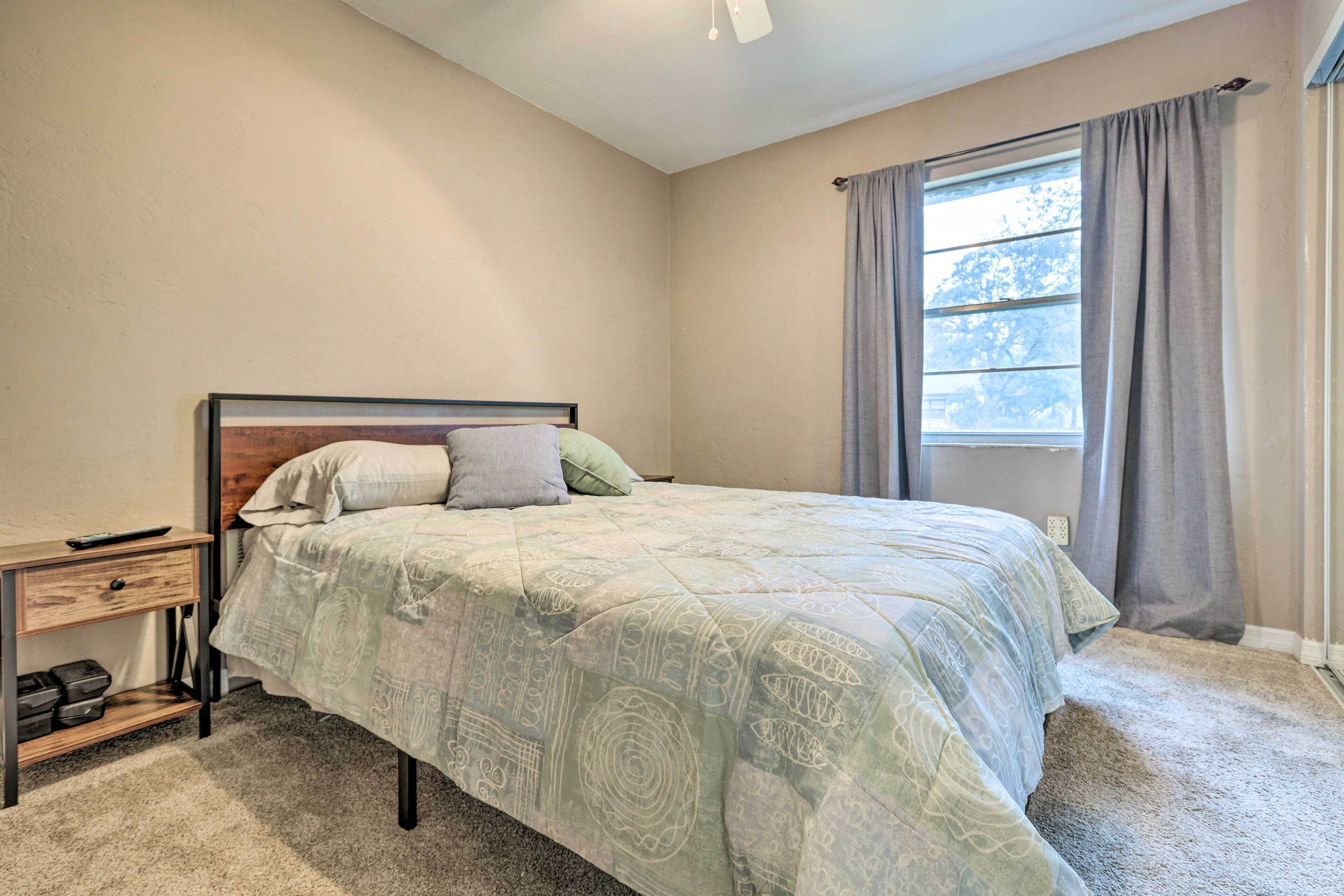 A bedroom with a bed, a nightstand, a window with curtains, and a carpeted floor.