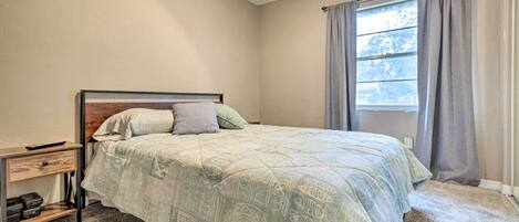 A bedroom with a bed, a nightstand, a window with curtains, and a carpeted floor.