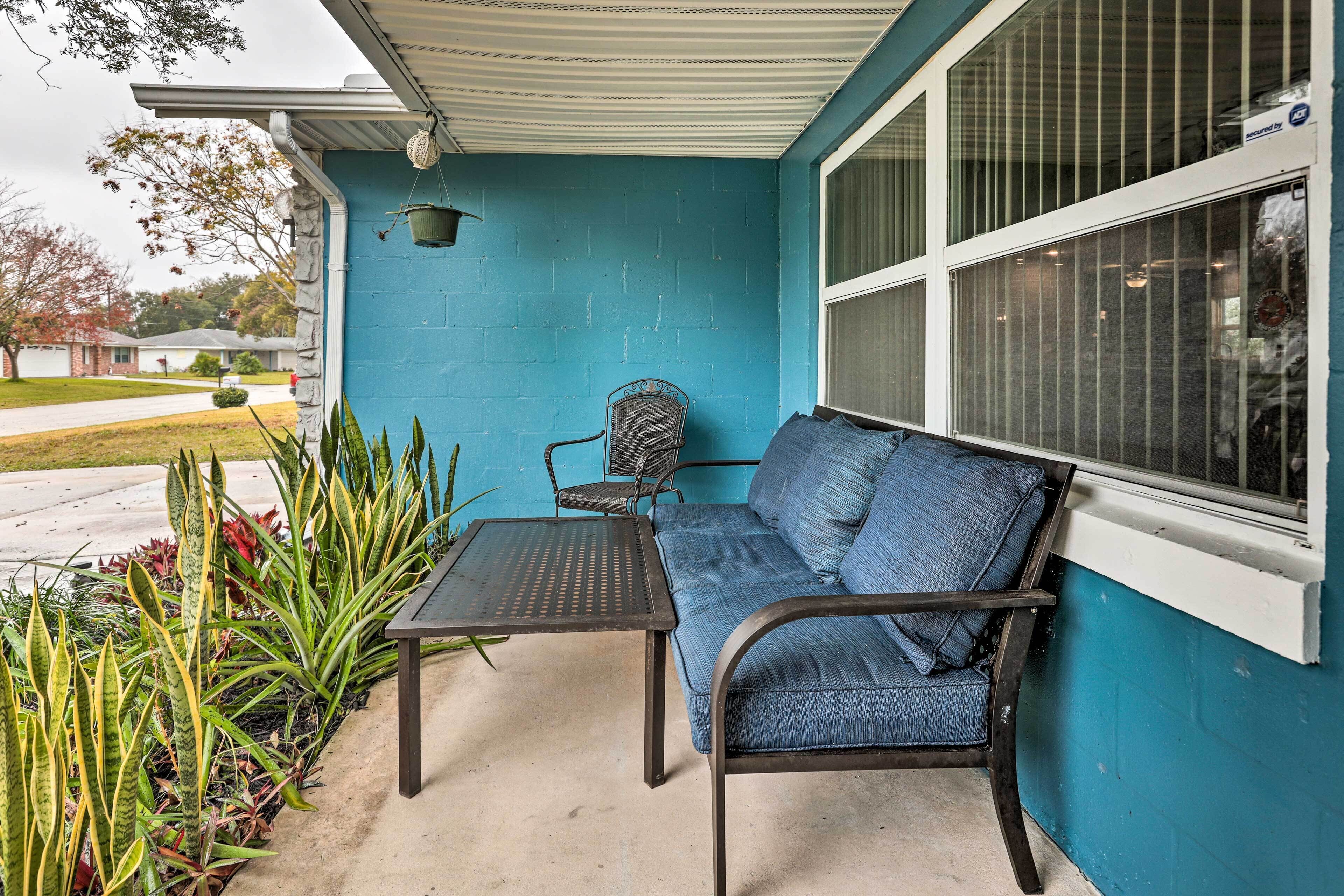 Une terrasse couverte avec un mur bleu, une table en métal, une chaise en métal et un canapé bleu.