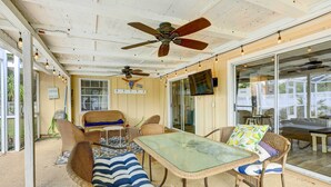 A covered patio area with wicker furniture, a glass table, ceiling fans, and a TV mounted on the wall. - Florida Vacation Rental w/ Screened Lanai (Ocala)