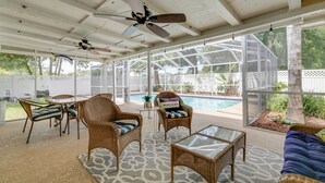 A covered patio area with wicker furniture, a glass table, and a view of a swimming pool. - Florida Vacation Rental w/ Screened Lanai (Ocala)