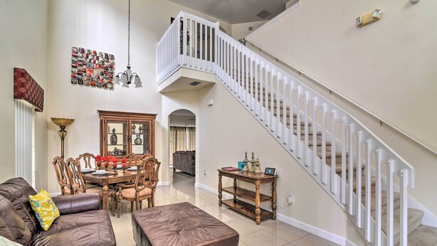 A spacious living room with a brown leather sofa, a wooden dining table, and a staircase with white railings. - ~ 9 Mi to Disney: Family Home w/ Private Pool! (Davenport)