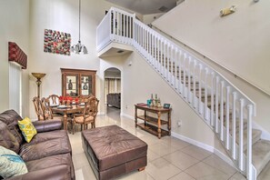 A spacious living room with a brown leather sofa, a wooden dining table, and a staircase with white railings.