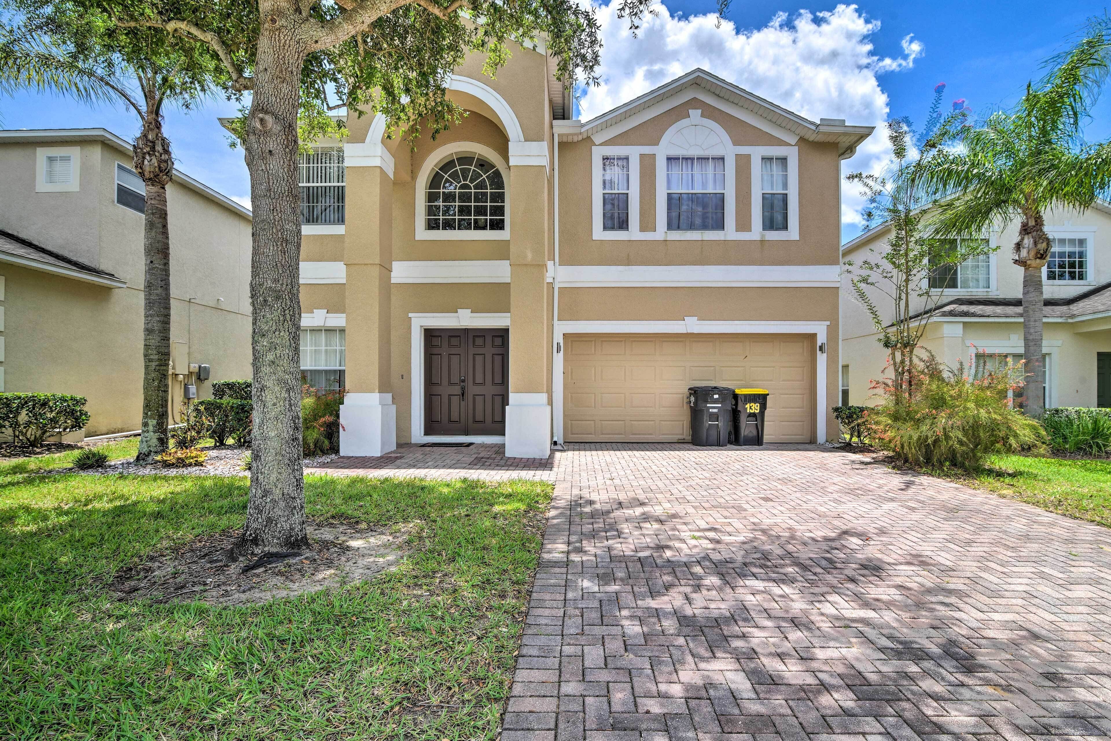 A two-story residential building with a beige facade, a central arched window, and a garage.