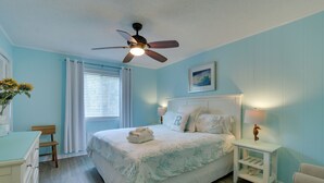 A bedroom with a bed, a nightstand, a chair, a desk, a ceiling fan, and a window with curtains. - Steps to Beach, Coligny Plaza: Hilton Head Condo! (Hilton Head Island)