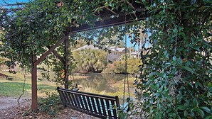 A wooden swing bench under a pergola with a view of a lake and houses in the background. - Steps to Beach, Coligny Plaza: Hilton Head Condo! (Hilton Head Island)
