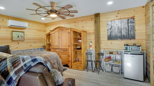 Une chambre confortable dans un chalet en rondins, avec un lit, une armoire en bois, une kitchenette et un ventilateur de plafond.