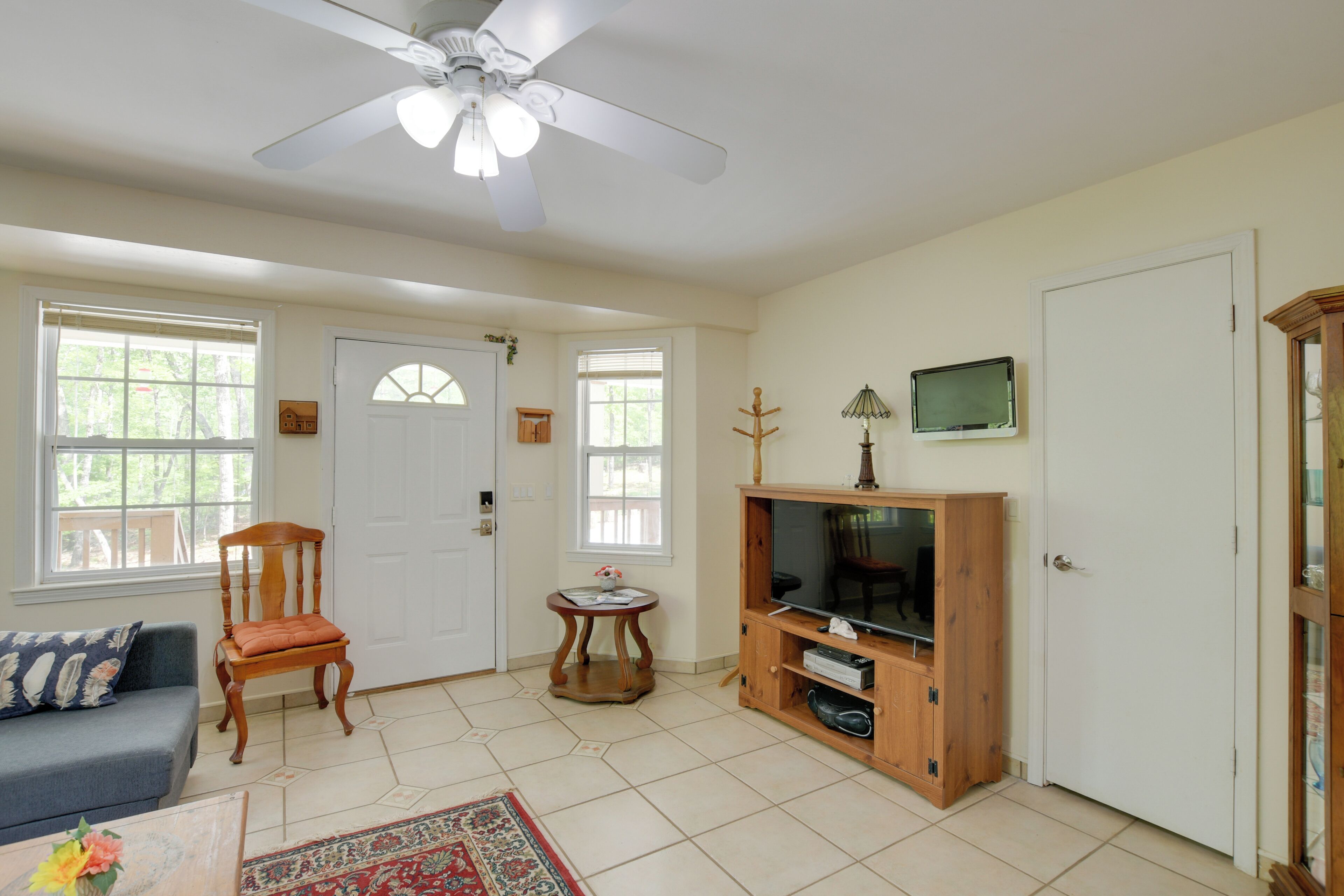 A living room with a ceiling fan, a wooden cabinet with a television, a blue sofa, and a wooden chair.
