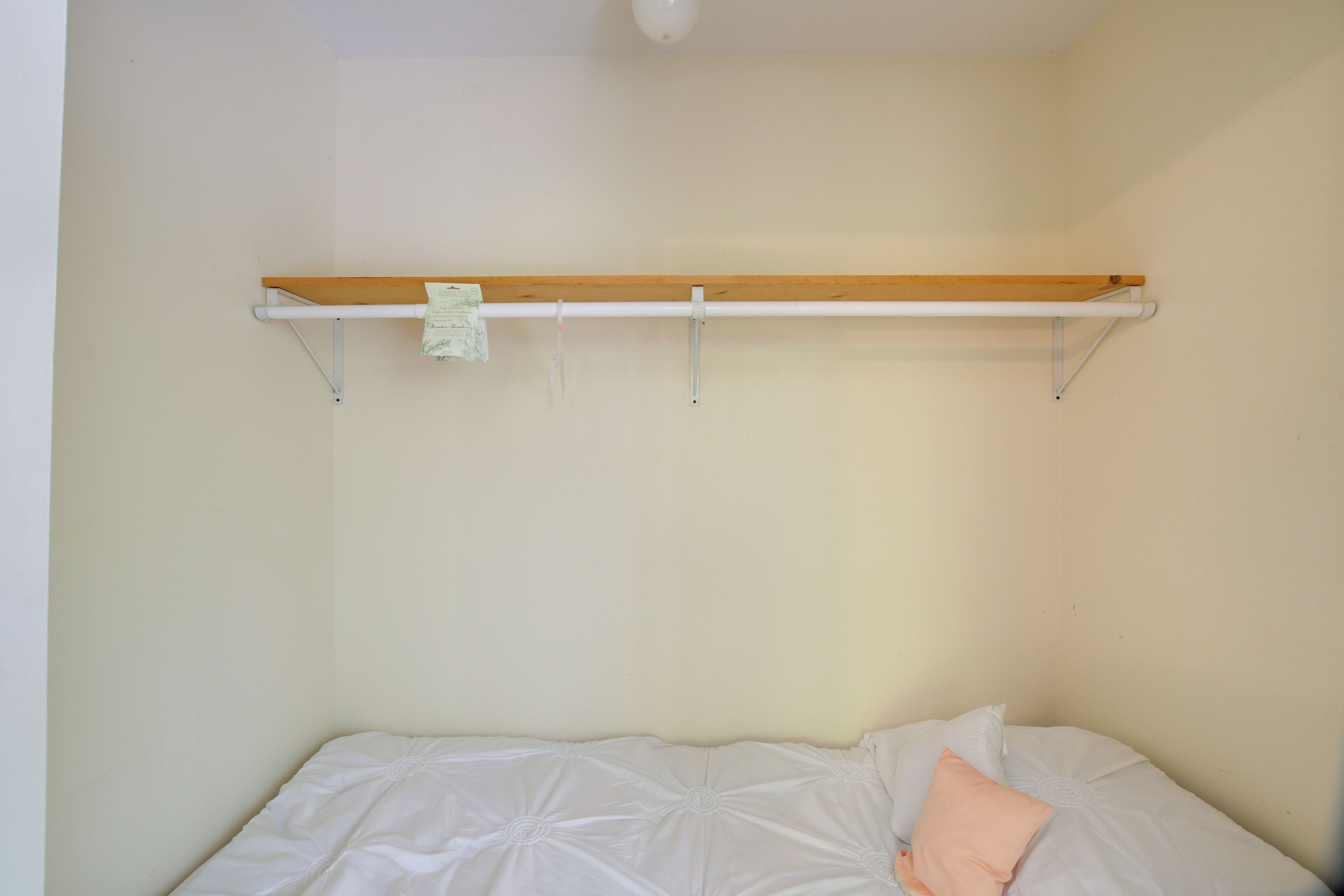 Een enkel bed met een houten hoofdbord, een witte matras en een perzikkleurig kussen.