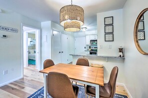 A dining area with a wooden table and chairs, a woven pendant light, and a kitchen in the background.