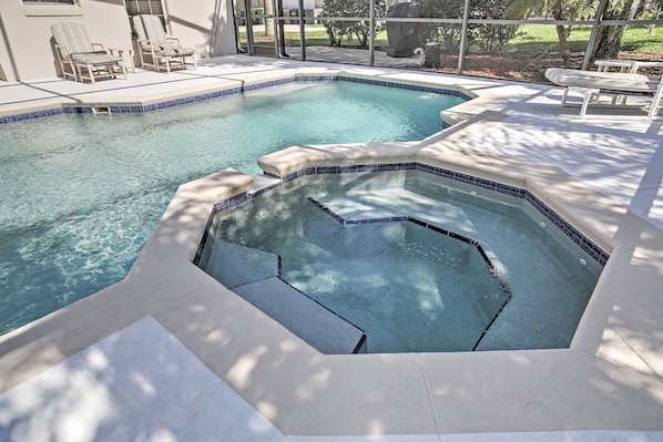 Una piscina con un jacuzzi, rodeada de sillas de descanso y una zona de patio techada.