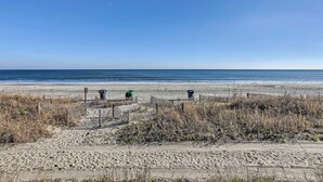 A sandy beach with a wooden fence and trash bins.